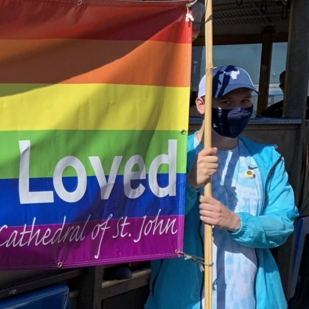 Person holding a rainbow “Loved” banner at Cathedral of St. John in a face mask