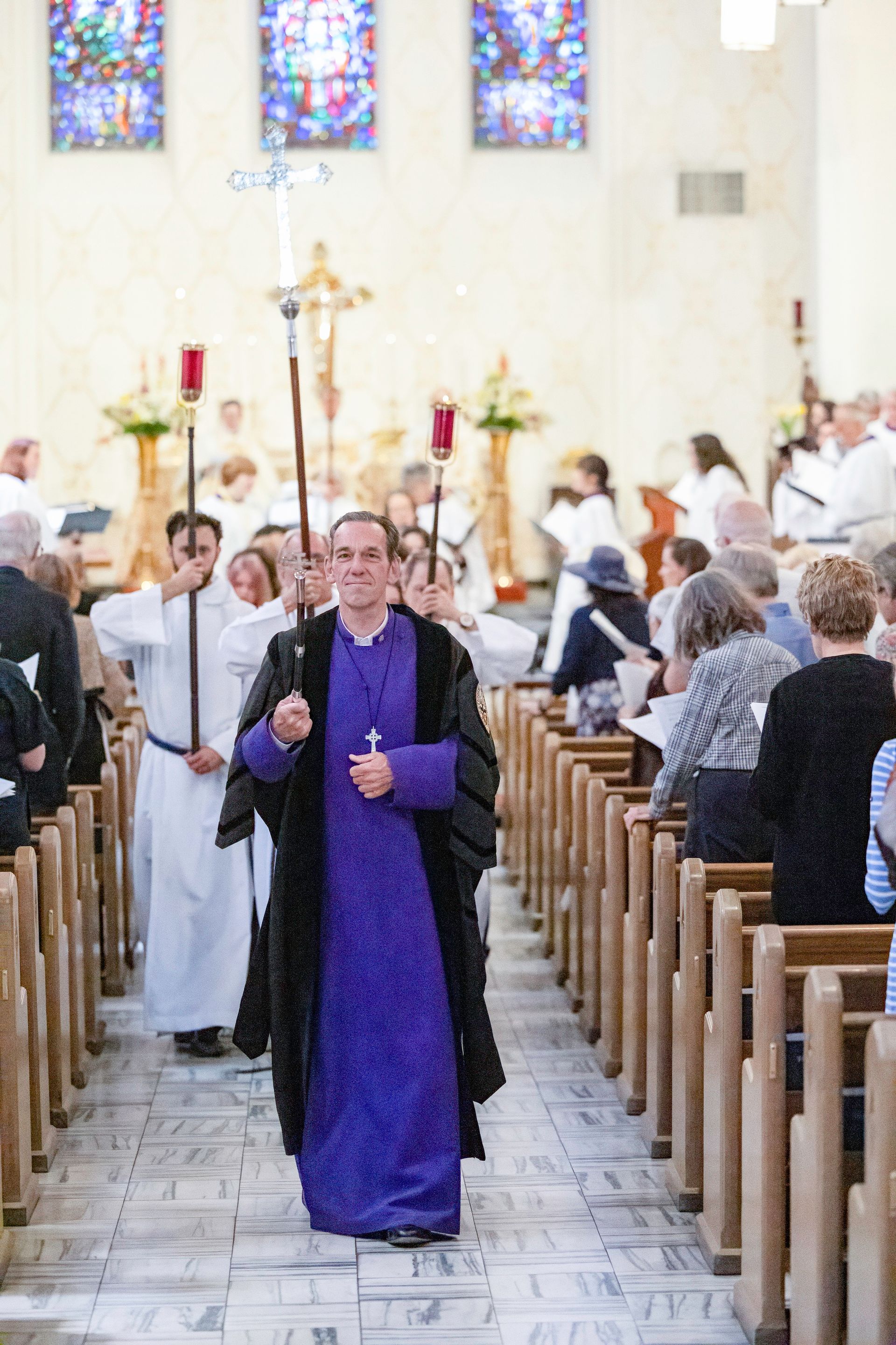 Clergy procession down church aisle,  carrying a cross.
