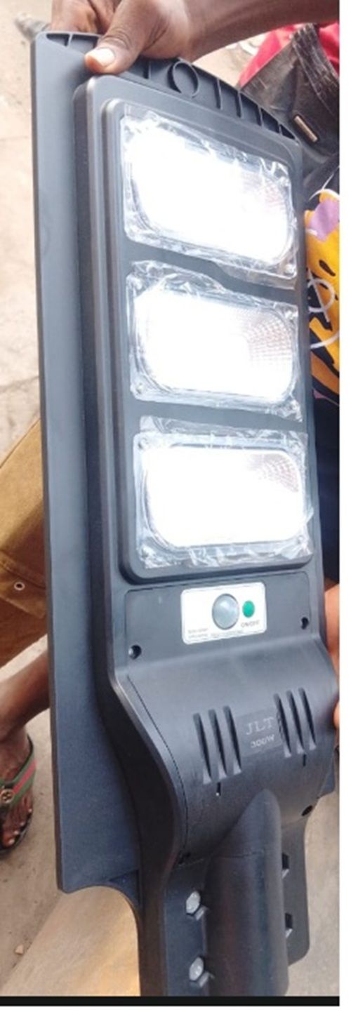 Black handheld solar LED street light with three lit panels, held outdoors by a hand.