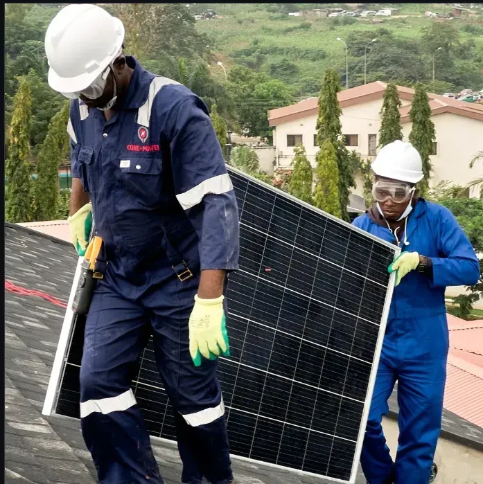 Workers installing a large solar panel on a rooftop in a green hillside area