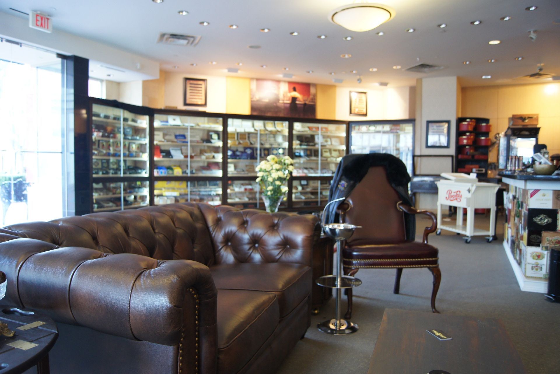 Cozy café lounge with brown leather sofa, chairs, and display cases behind the counter