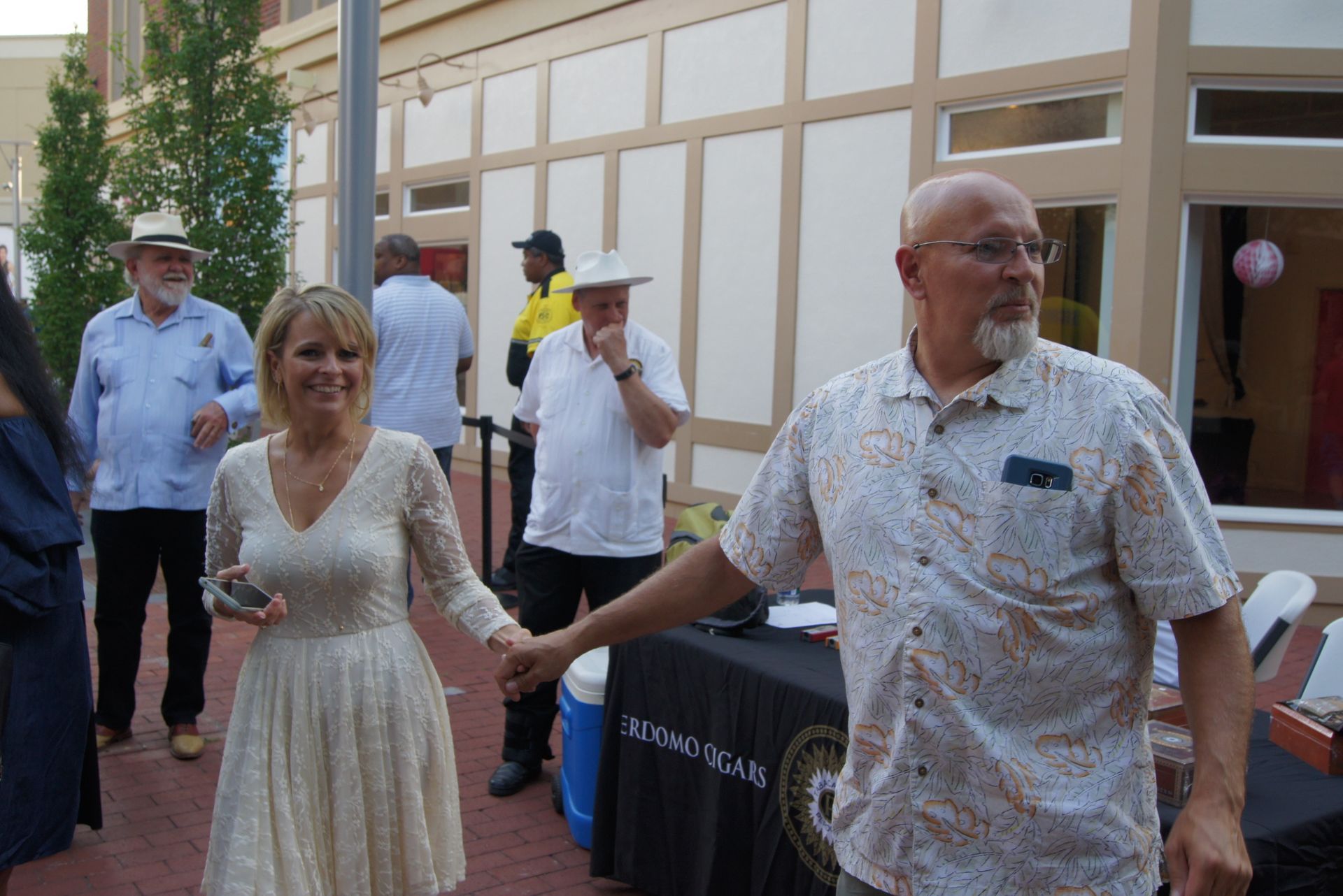 People walking outdoors near a building, holding hands and smiling at an event table