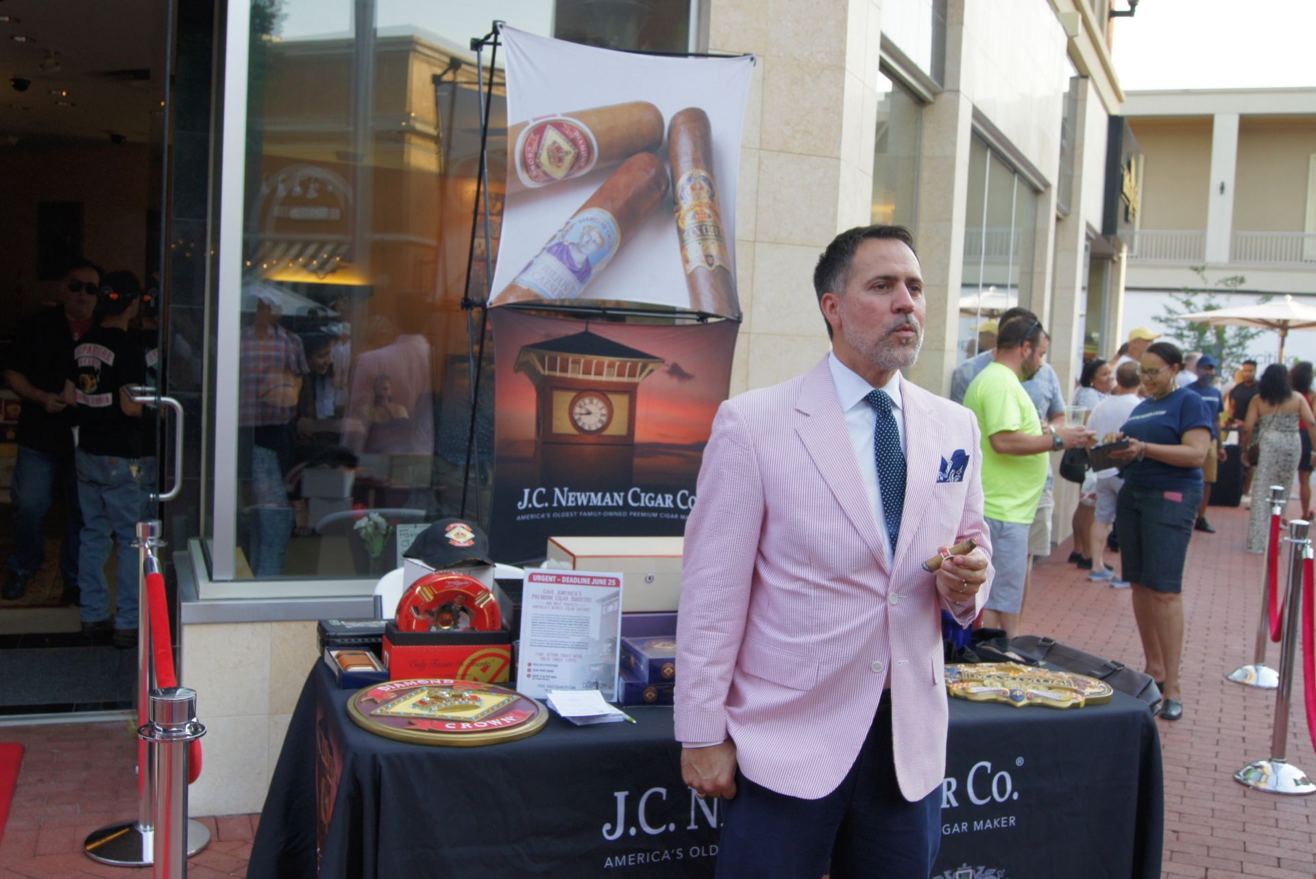 Man in pink blazer stands by a cigar booth at an outdoor market