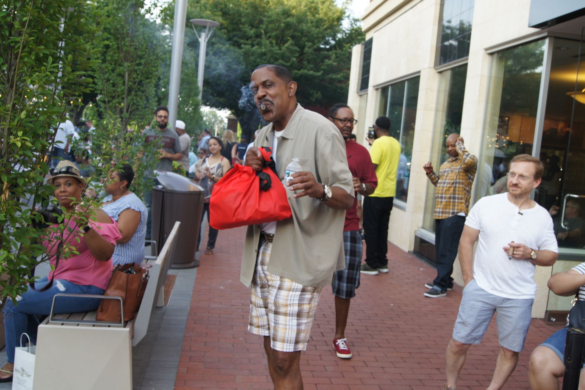 People standing outside a building, some holding bags and drinks, on a brick patio.