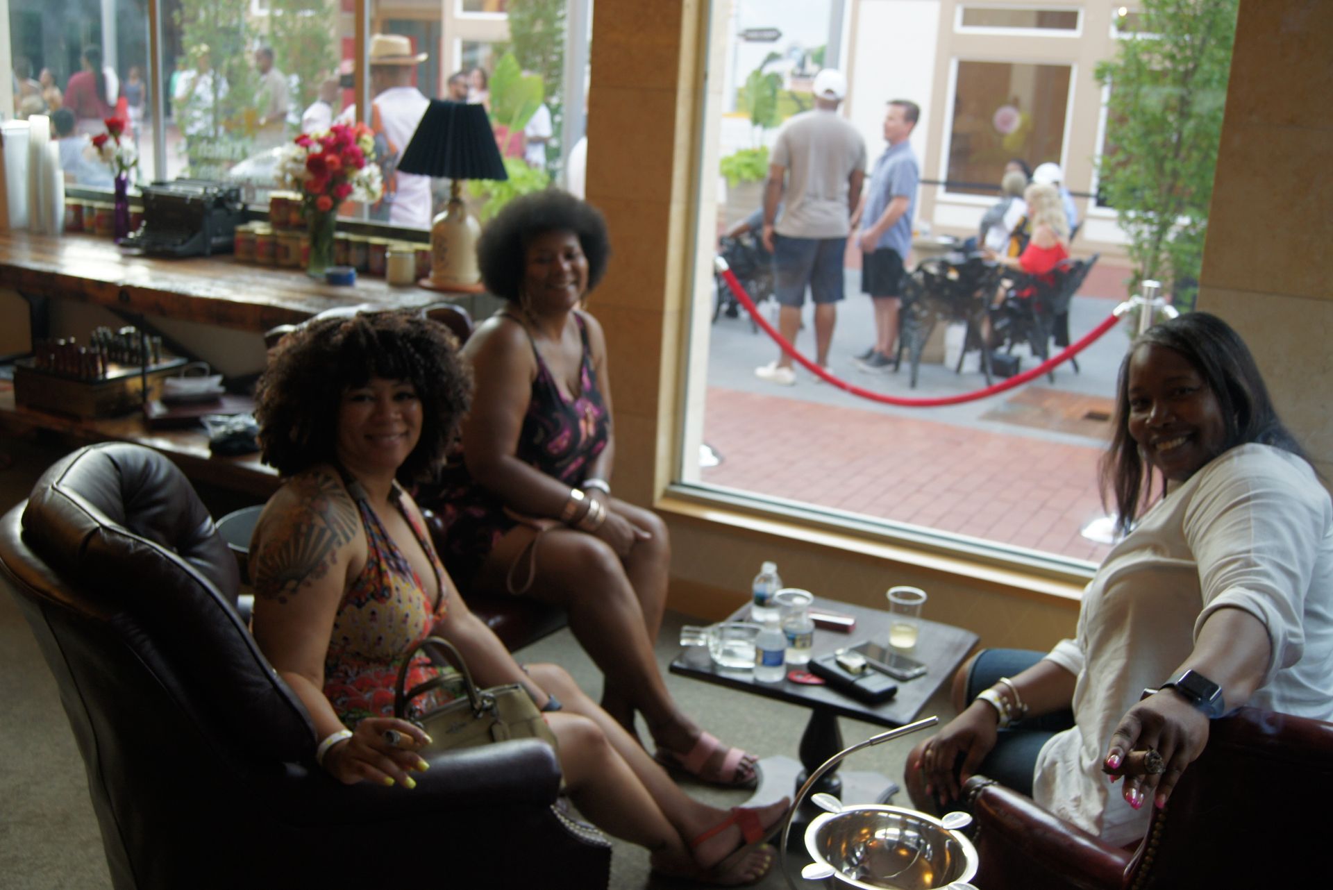Three people sitting in a lounge by a window, with drinks and a city street visible outside.