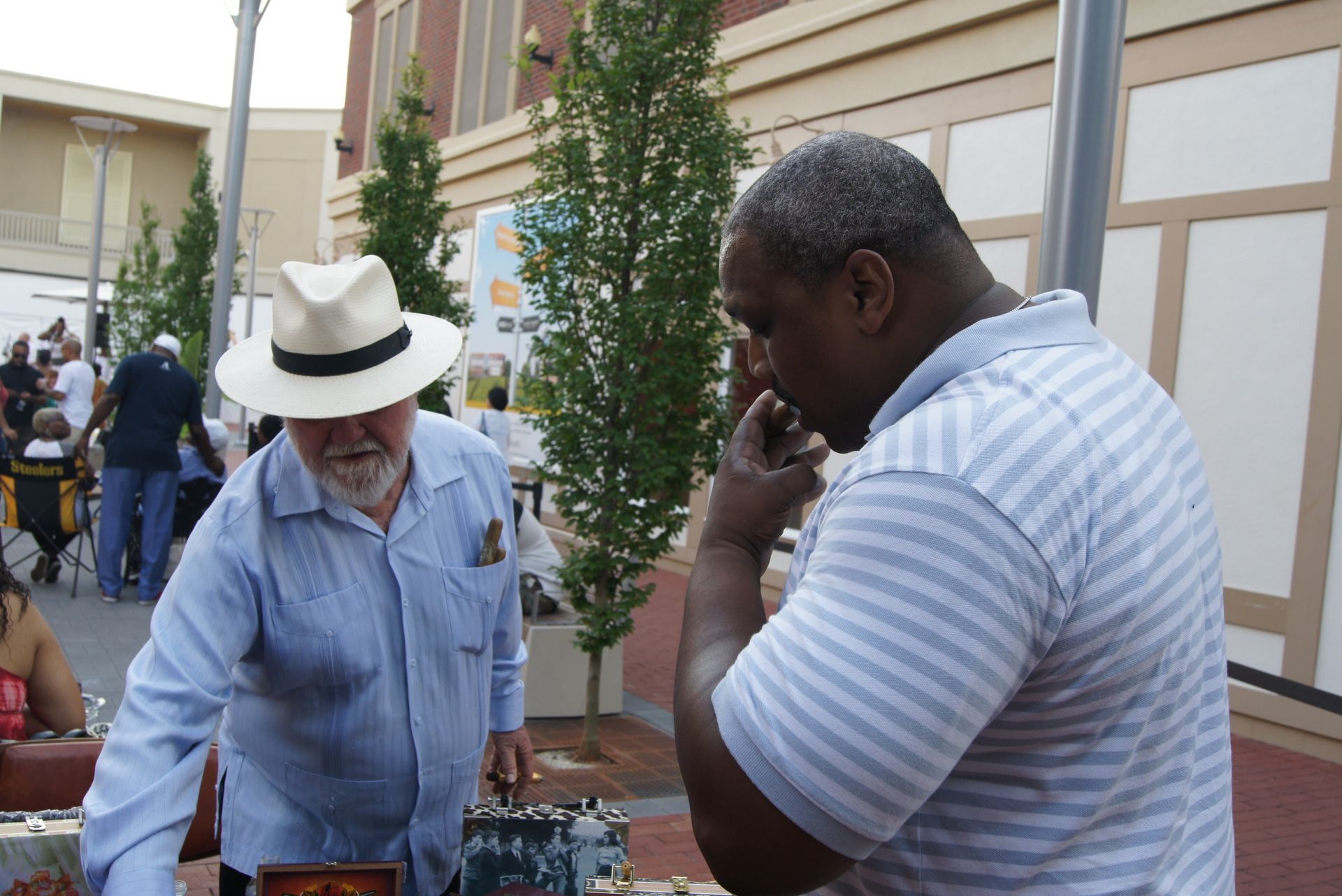 Two people at an outdoor market, one in a white hat, another speaking on a phone near a table