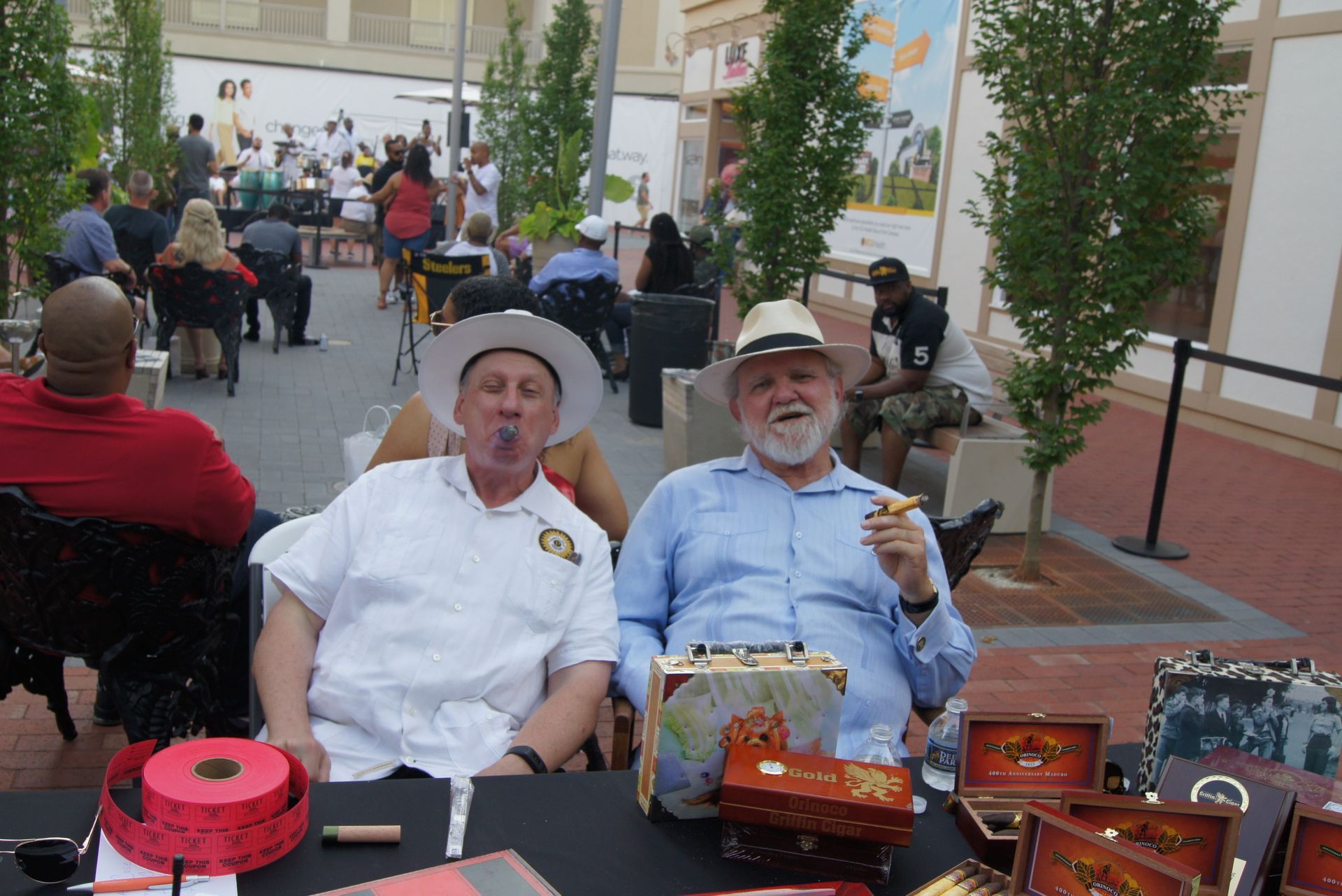 Two people seated at a market table with carved wooden crafts and colorful goods outdoors