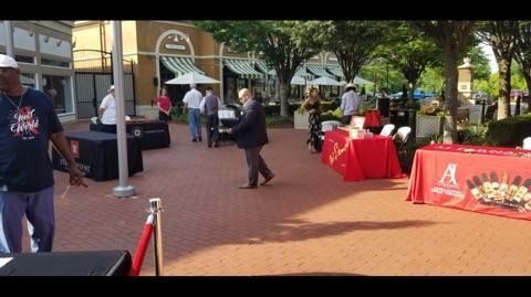 Outdoor plaza with vendor booths and red tablecloths, including a black-covered display and people walking nearby.