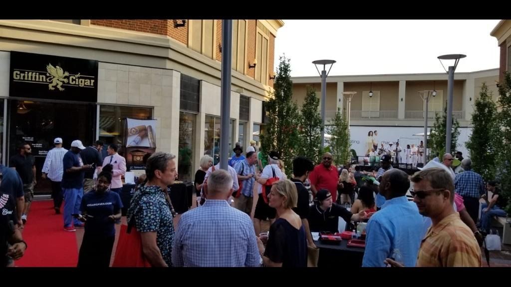 Crowd gathered on a red carpet outside a theater entrance, with storefronts and tall lamp posts nearby