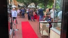 Red carpet leading to a crowd gathered outside a building with trees overhead.