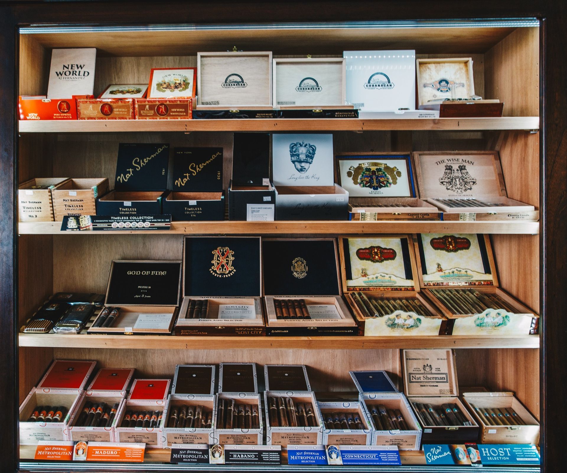 Wooden display case filled with assorted cigars in rows and colorful boxes
