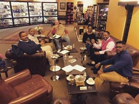 Group of people seated around a coffee table in a cozy lounge, chatting and enjoying drinks and snacks.