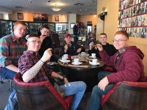 Six people seated around a café table, raising cups in a casual toast.