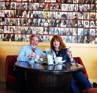 Two people smiling at a café table beneath a wall of portrait photos