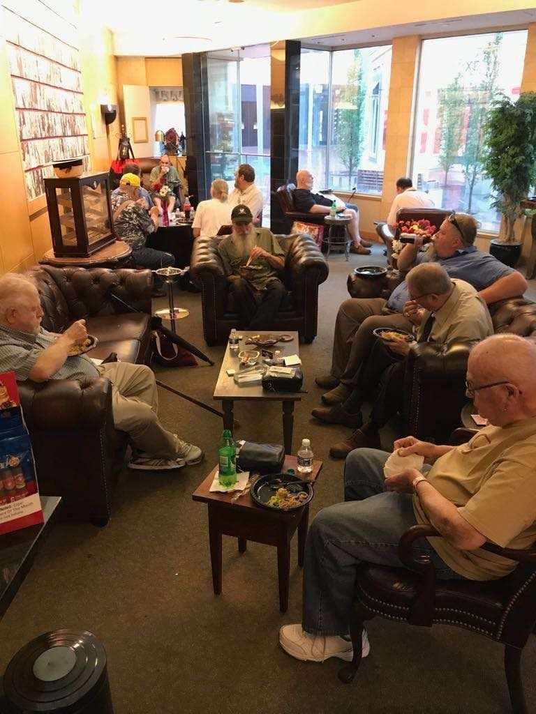 People seated in a cozy living room, chatting around a coffee table with snacks and drinks.