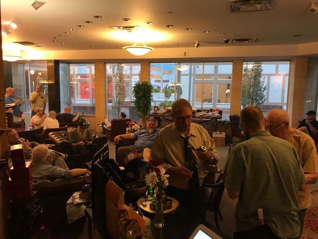 Crowded indoor lounge with people seated and chatting around tables under warm ceiling lights