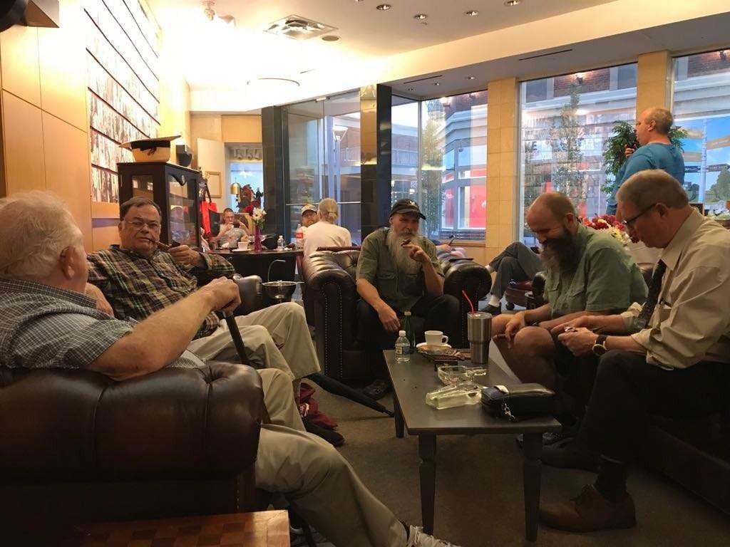 People seated in a bright lounge, talking and using laptops around a table.