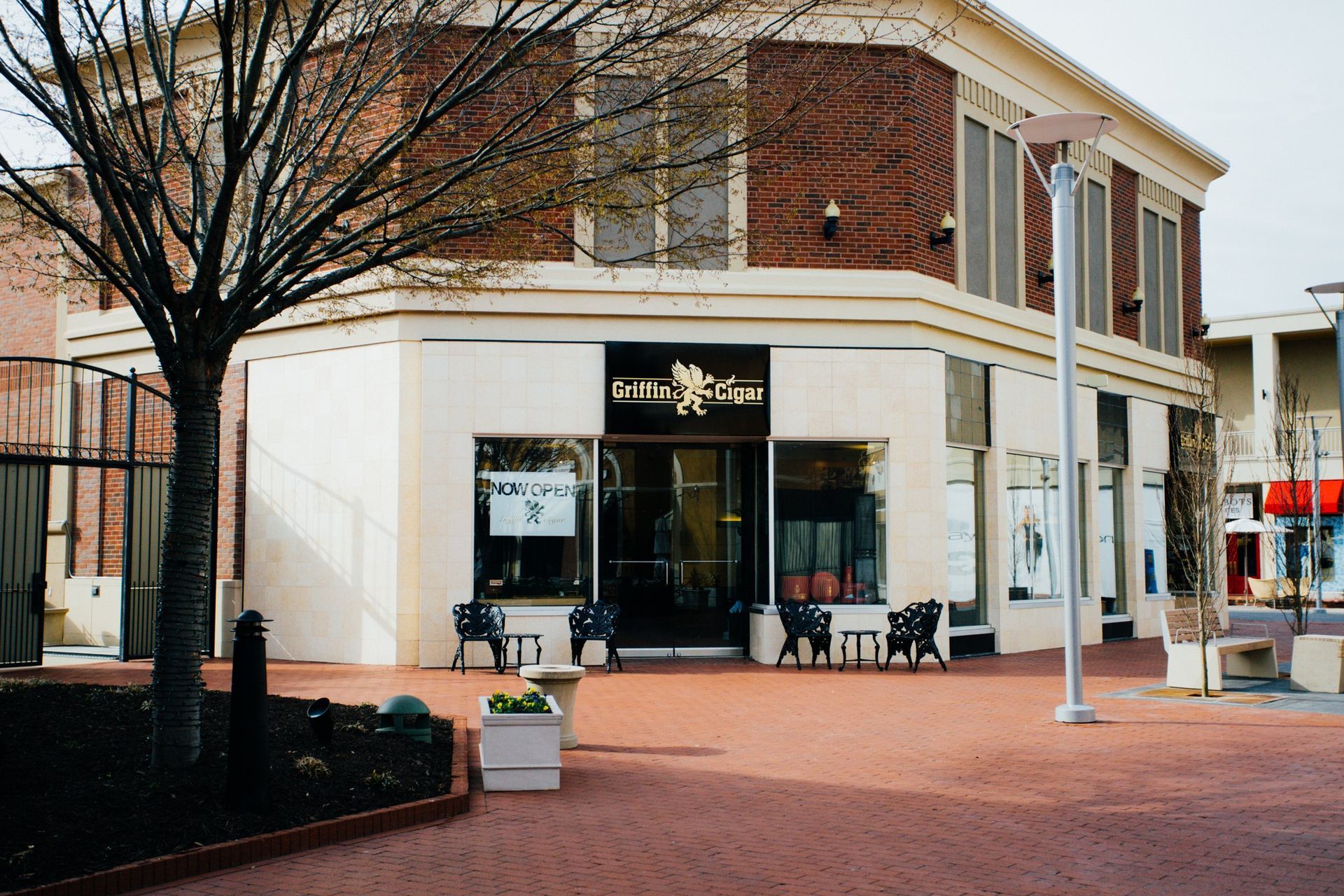 Corner storefront with white-and-brick facade on a brick-paved street, with a tree and benches outside