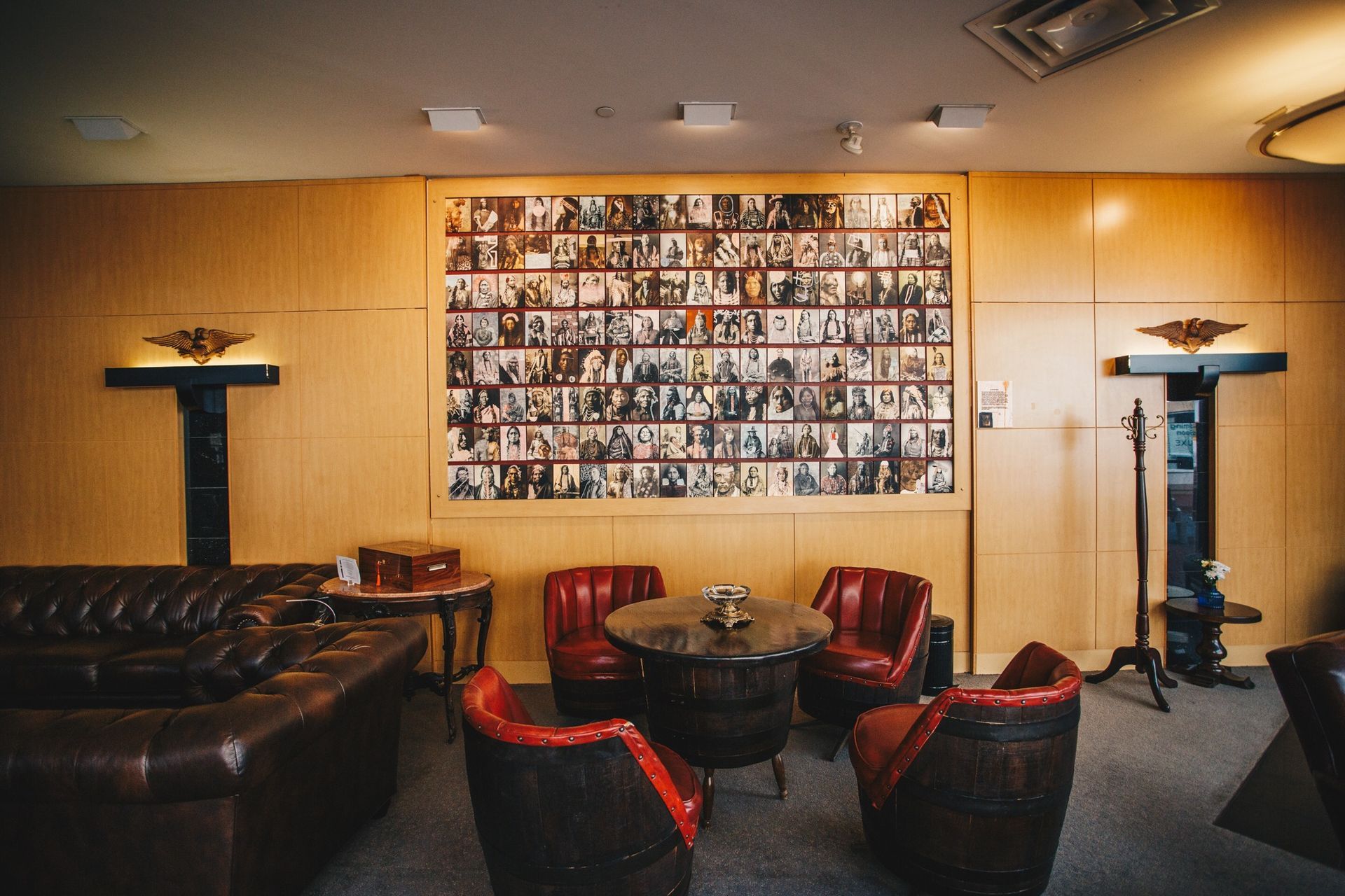Cozy lounge with leather chairs, small tables, and a large wall collage of many photos.