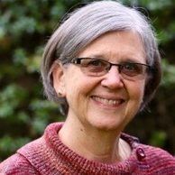 Woman with gray hair and glasses smiling outdoors in a red sweater.