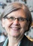 Woman with short gray hair, glasses, smiling, wearing a black blazer and blue shirt.