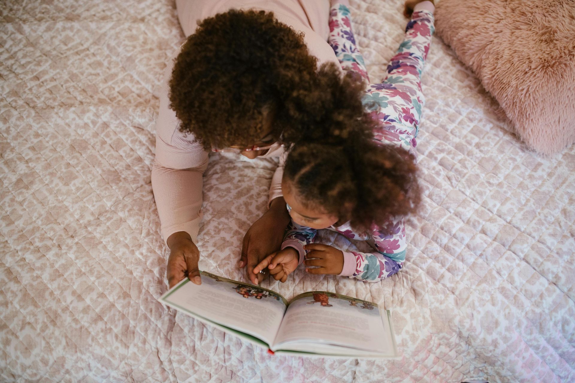 Woman and child reading a book together on a bed.
