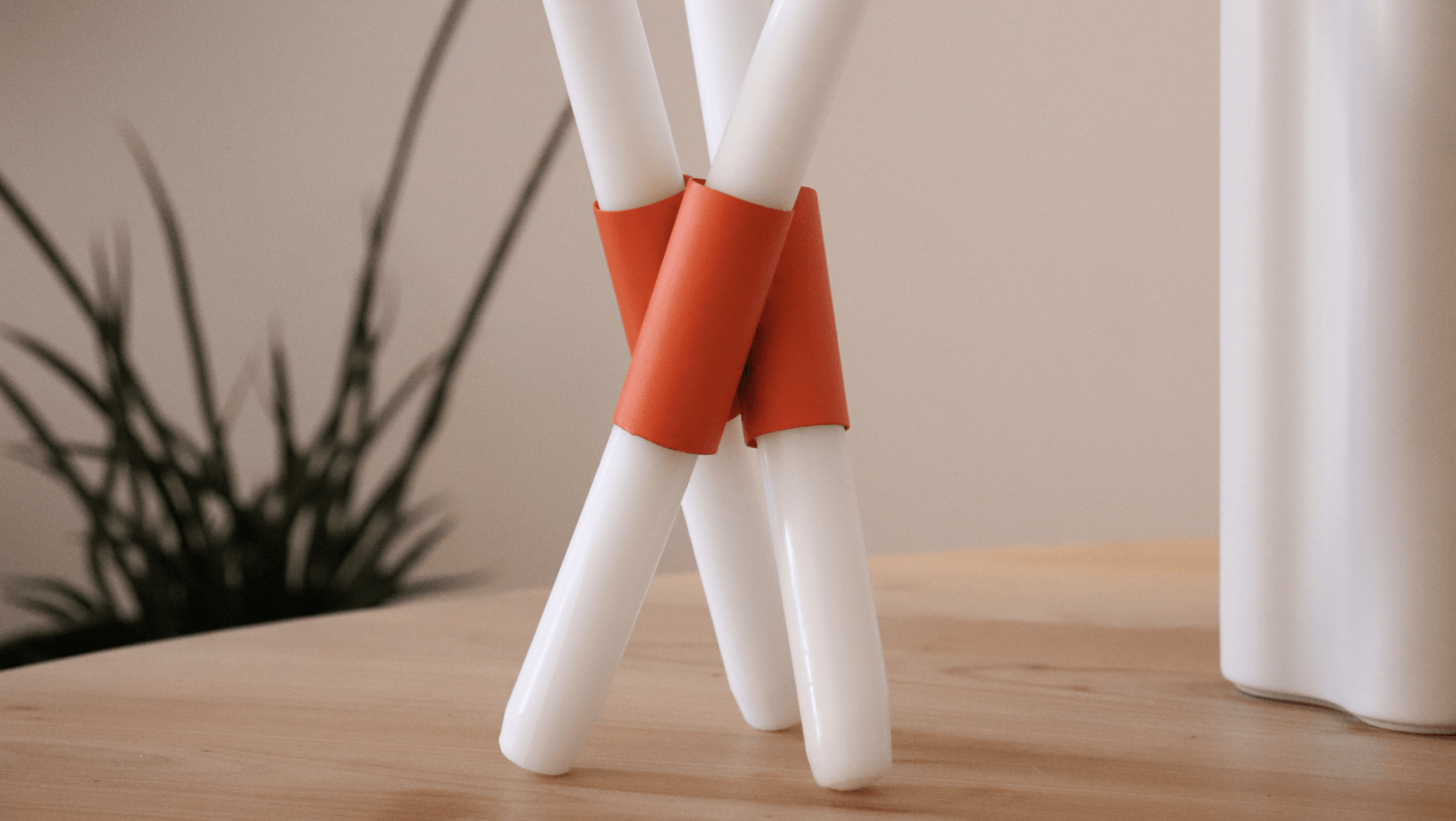 Tres velas blancas están sobre una mesa de madera. Mersi Studio