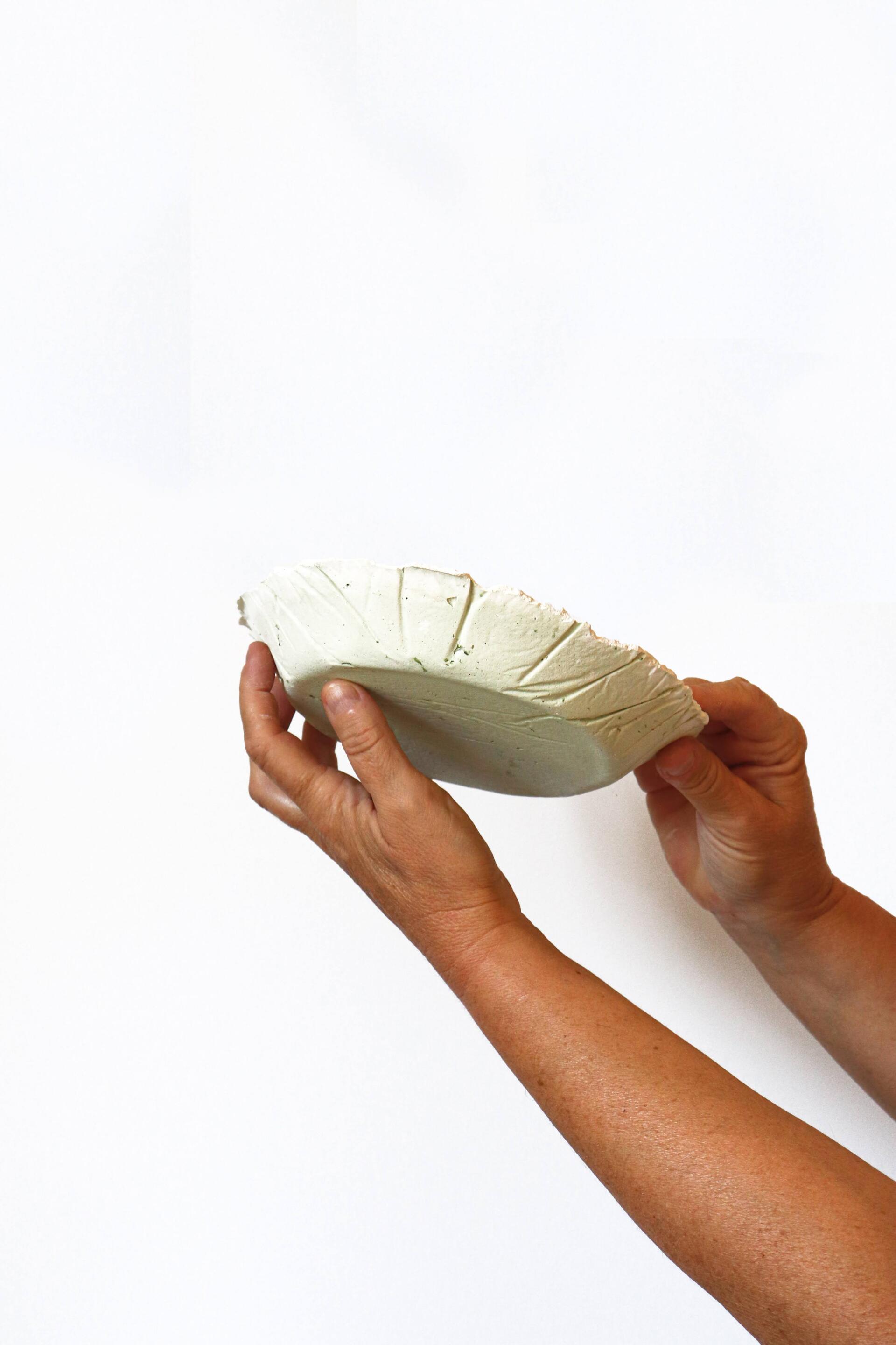 Fotografia dels productes final del projecte egg dishes fets amb biomaterial. Mà agafant els plats i ensenyen-los per tots els angles. Dissenyat per mersi studio.