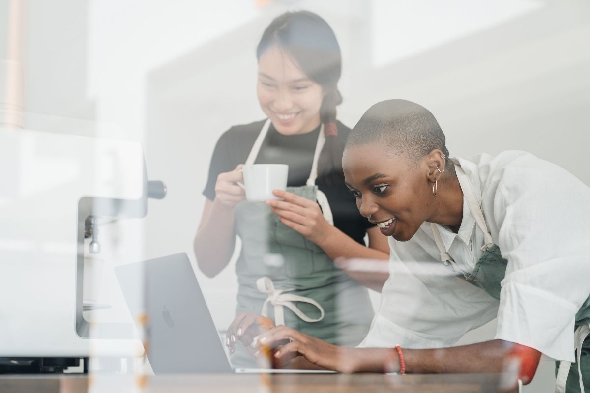 Two young female baristas using laptop to get their cafe ready for the use of AI in business.