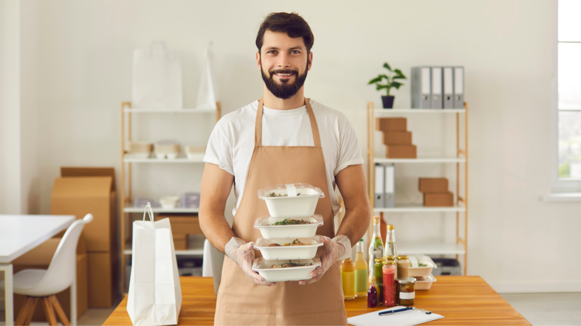 A franchise owner in an apron is holding a stack of plastic containers