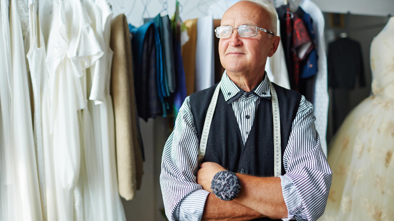 An older man is standing with his arms crossed in a clothing store.