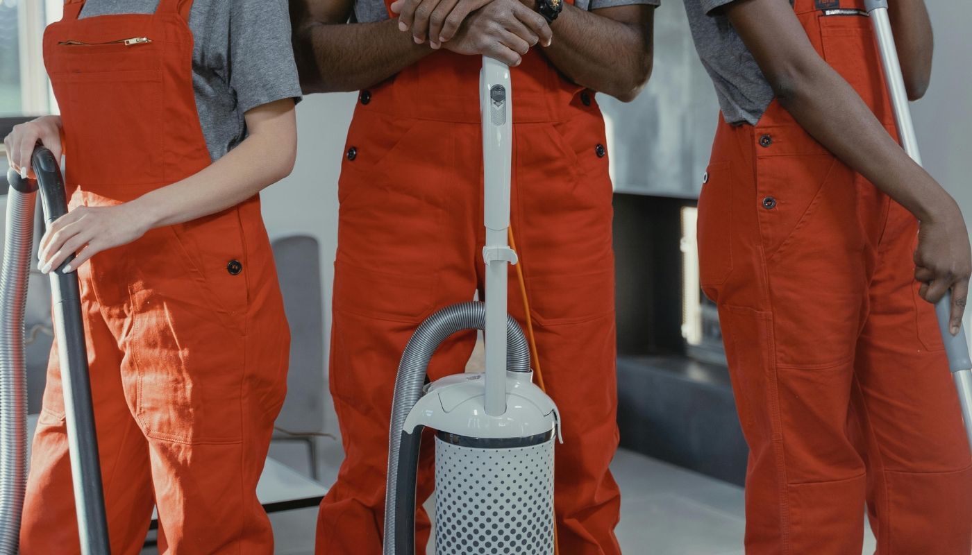 Three workers of one of the best franchise industries in red coveralls with cleaning tools in a room.