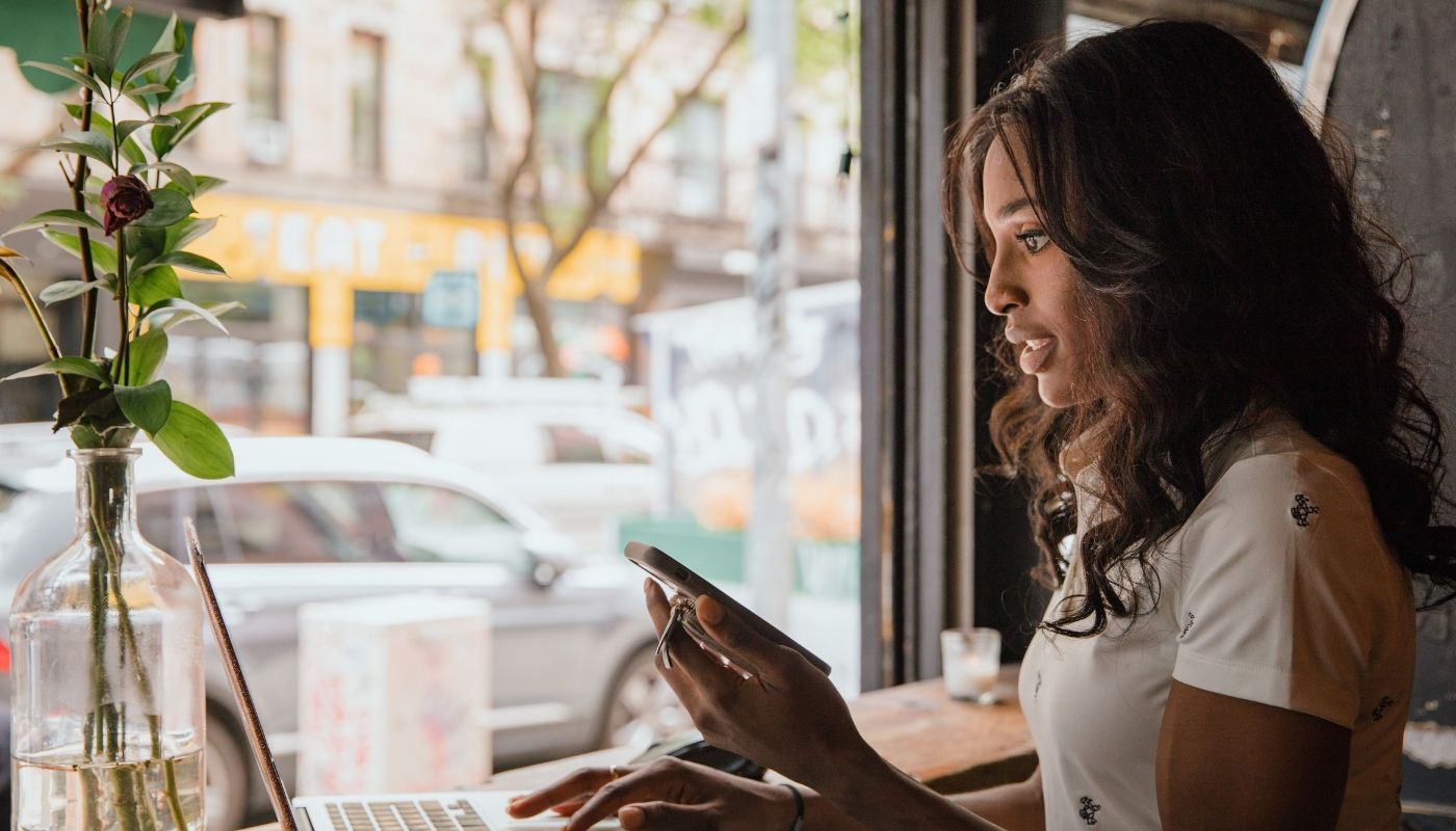 Woman working remotely on a laptop and phone during a franchise advisory consultation in an urban café setting