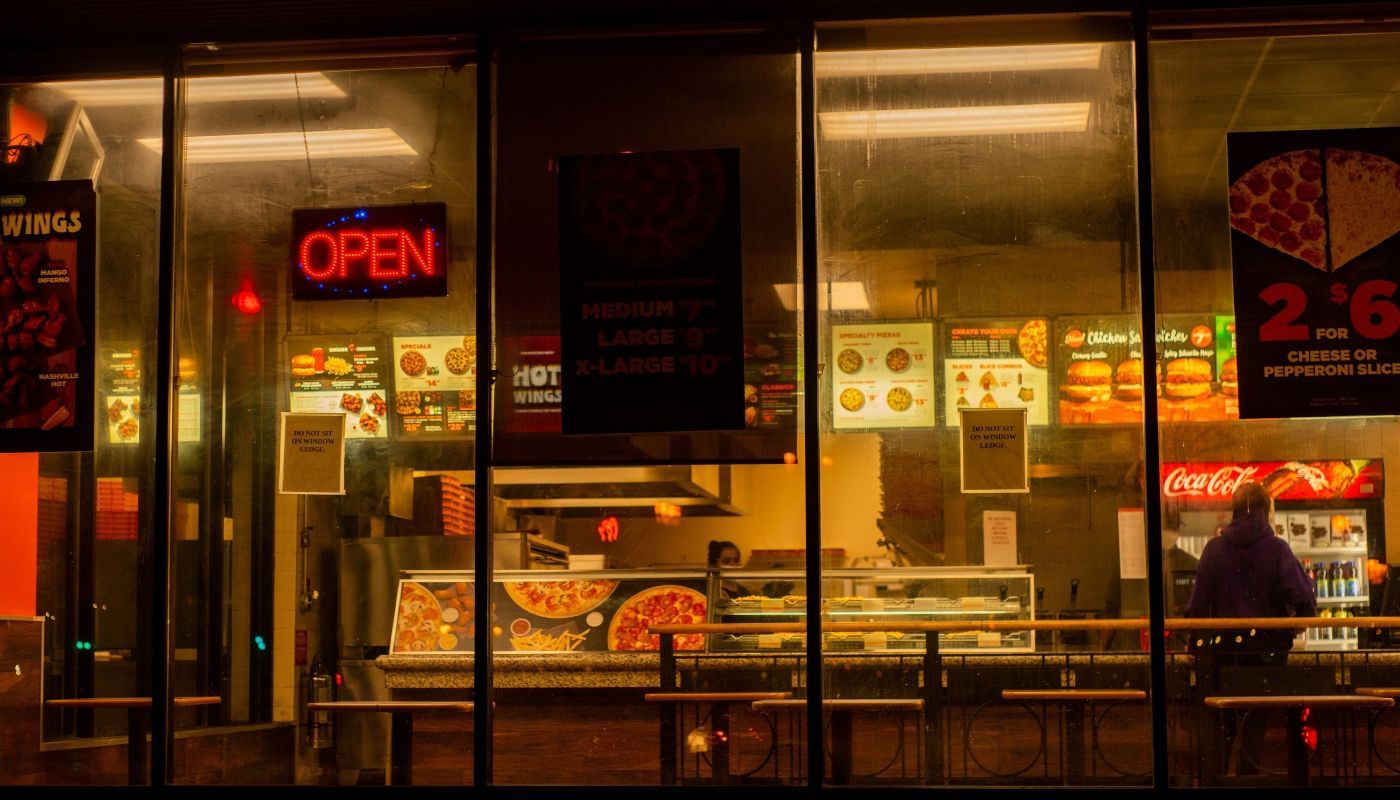 View of a pizza restaurant through a glass window at night, showcasing a local franchise business in operation.