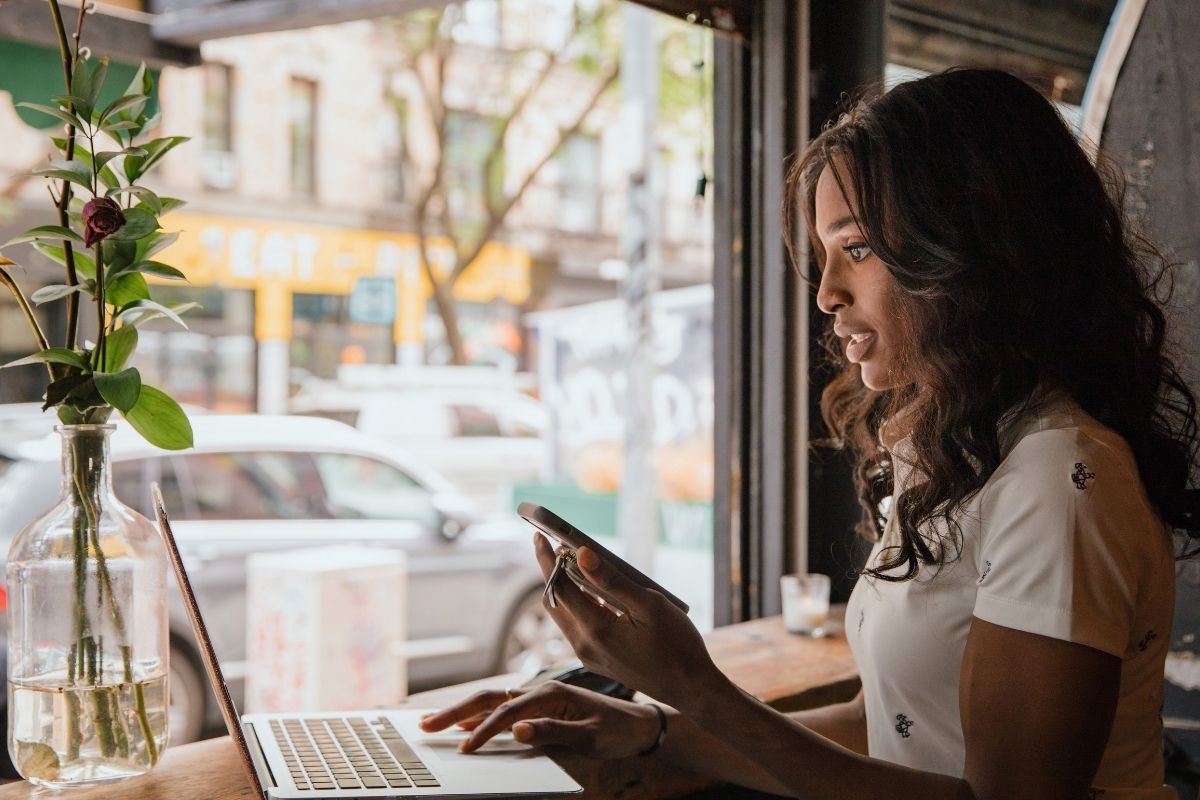 Woman in a cafe, using her laptop and phone to interview possible franchise employees