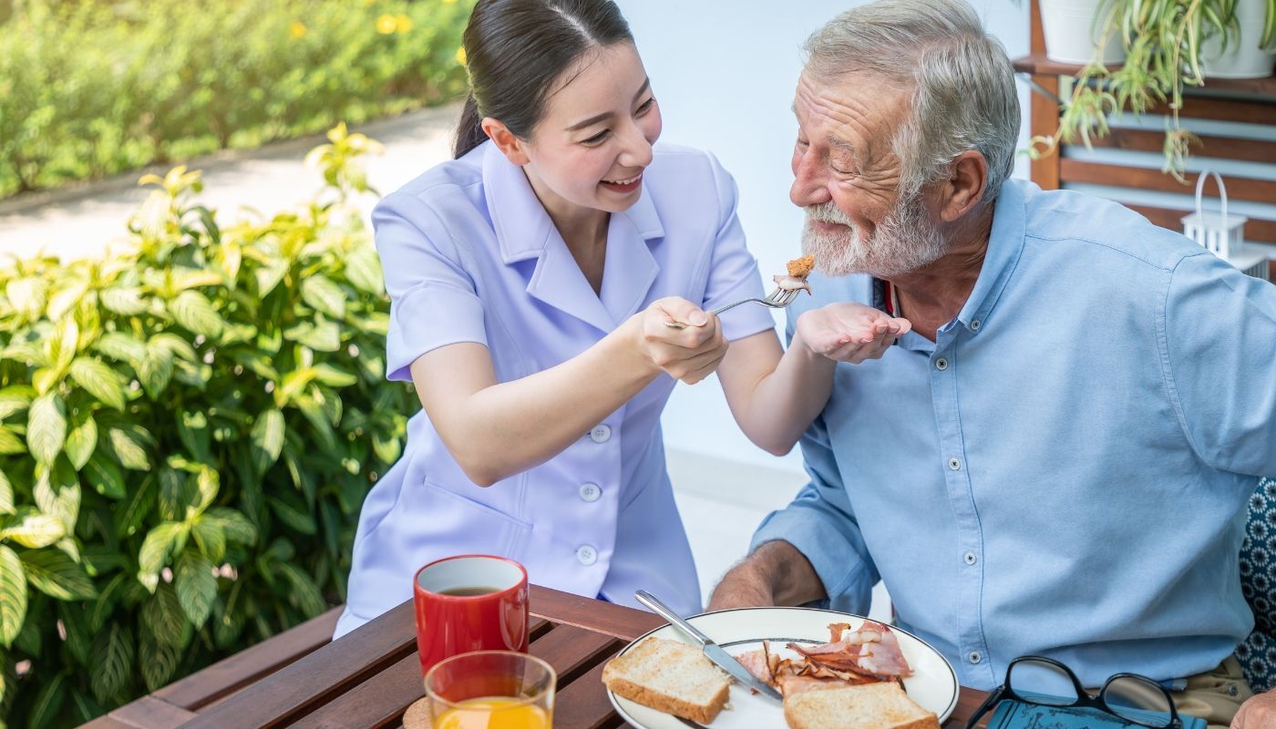 Home care nurse feeding senior man while providing services through growing mobile franchises businesses