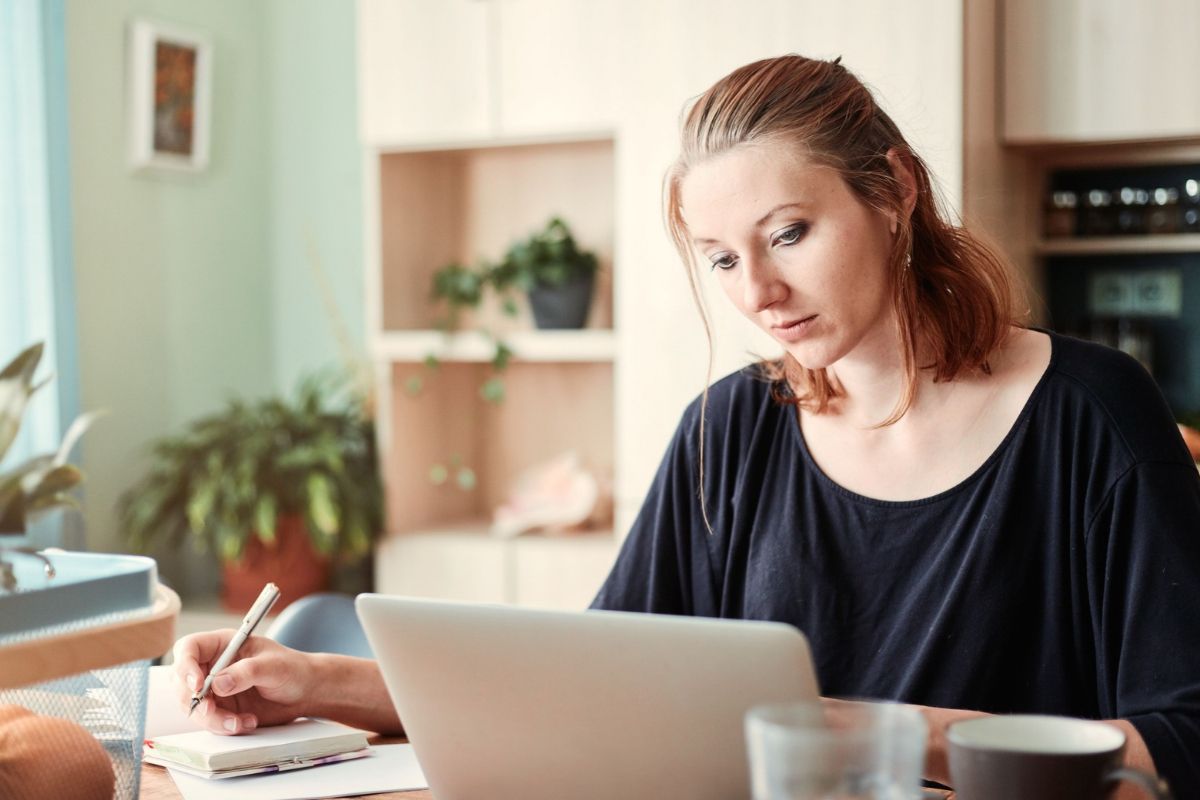 Woman working on laptop in home office, taking notes on common myths about owning a franchise