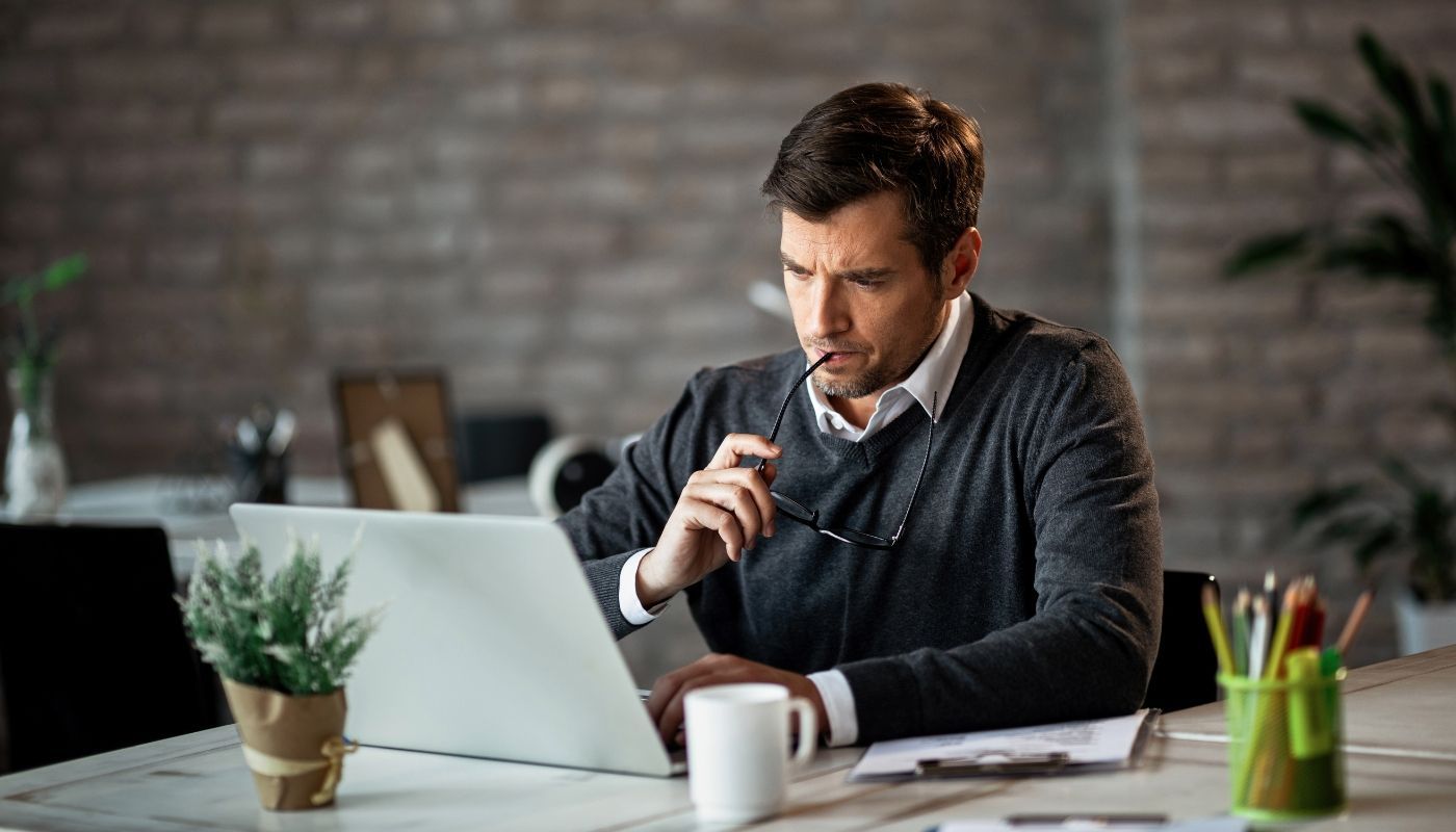 Serious businessman using a computer while reviewing the risks of owning a franchise and business performance data.