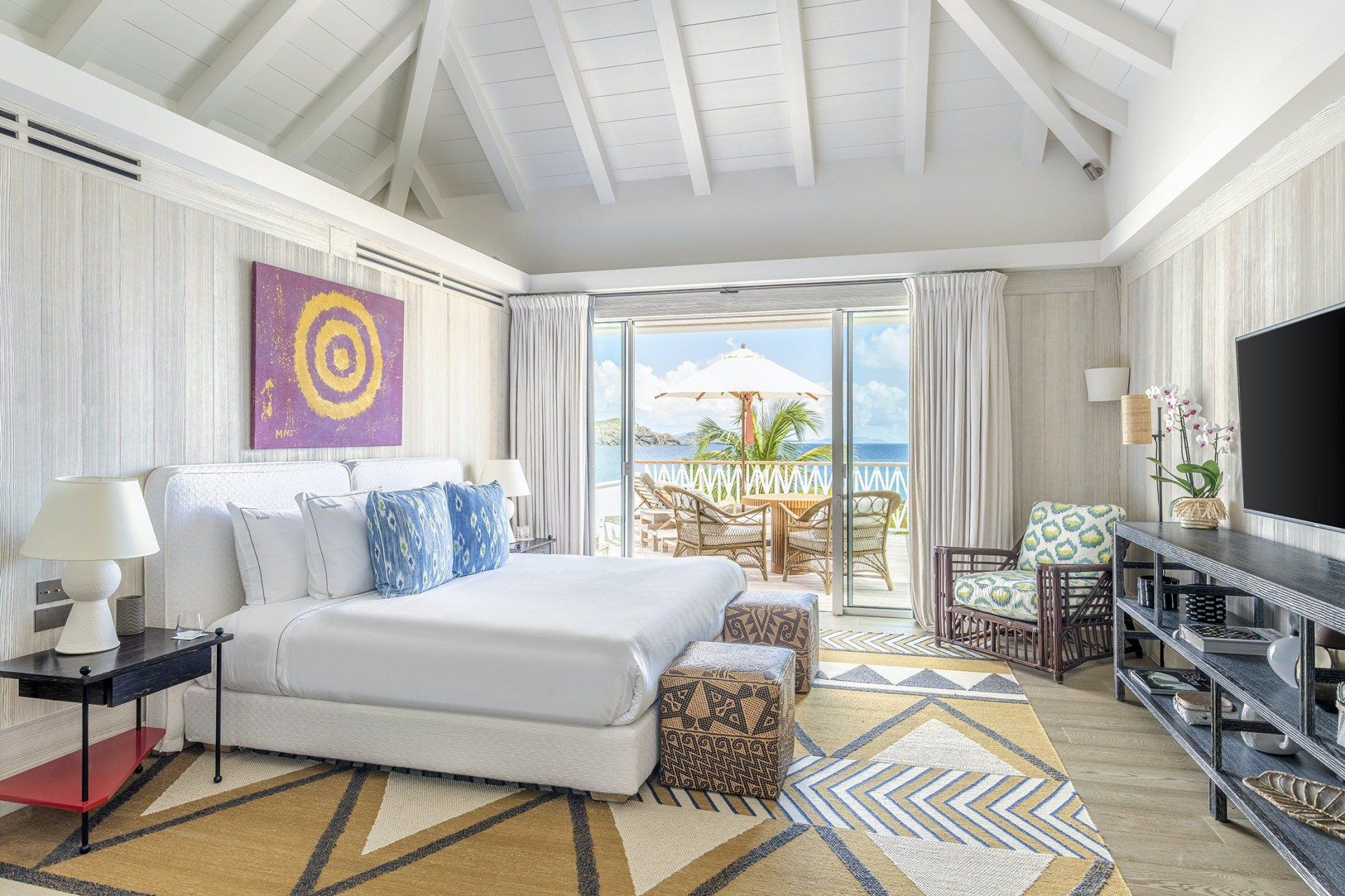 Bedroom with a white bed, doors to a beach patio, and a patterned rug.