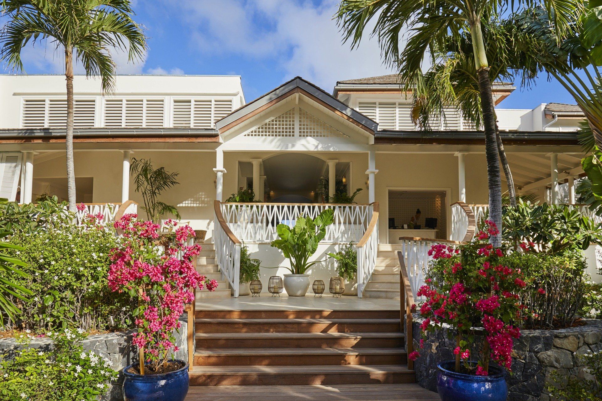 Exterior of a white building with a veranda, steps, and tropical landscaping.