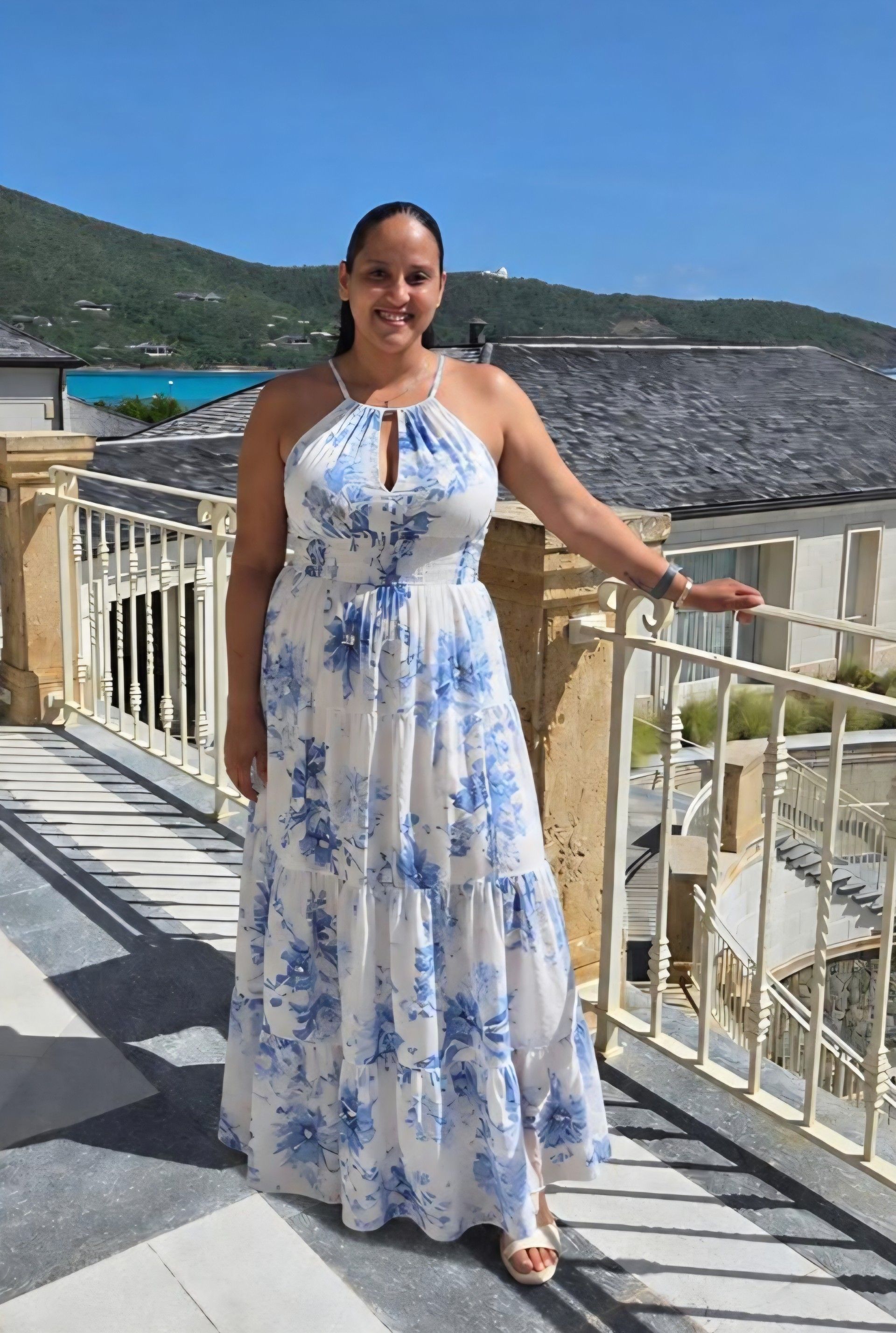 Woman posing in a white floral dress in front of a black fireplace and ornate wall art.