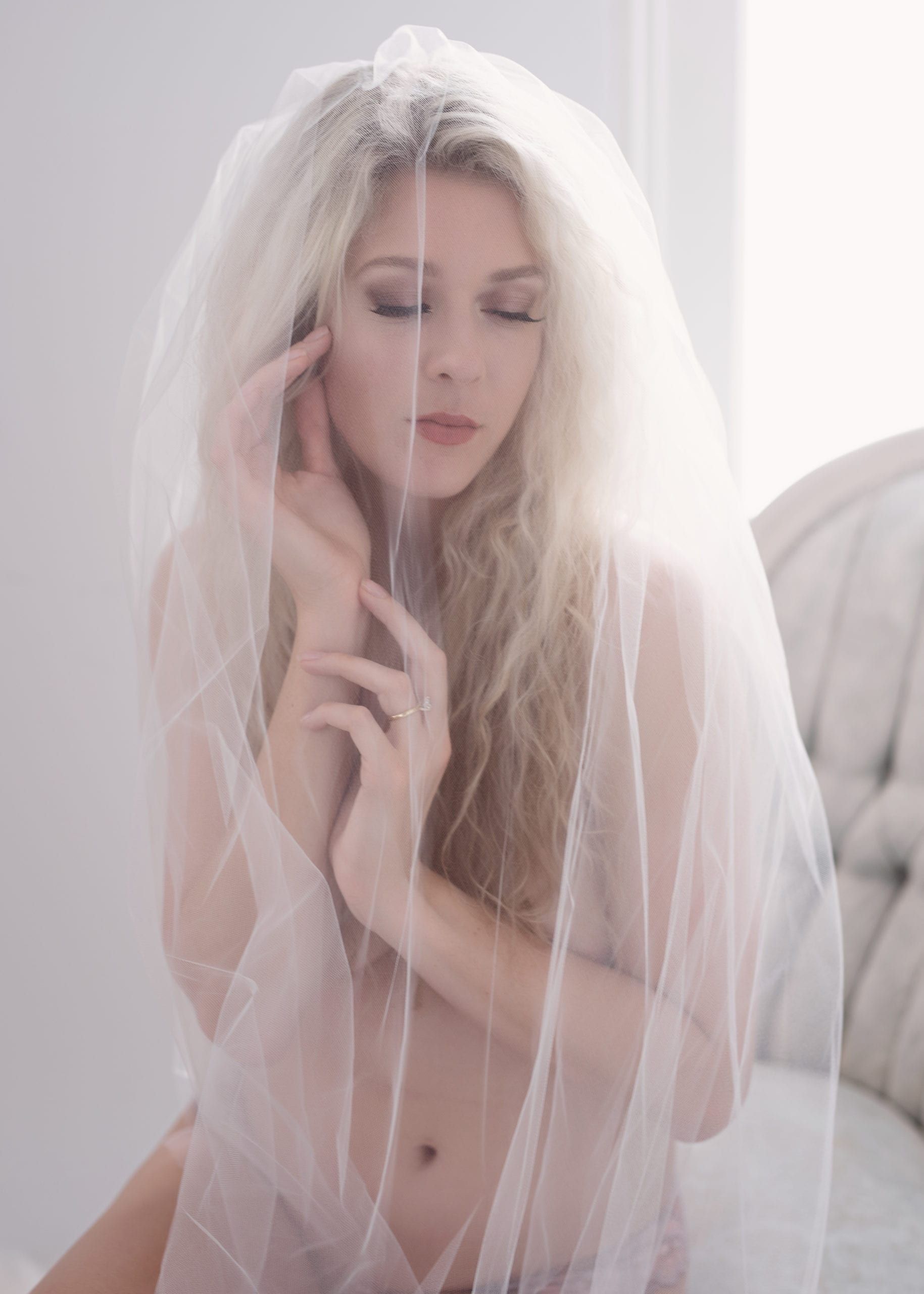 Woman veiled in white, hands near face, eyes closed, soft lighting.