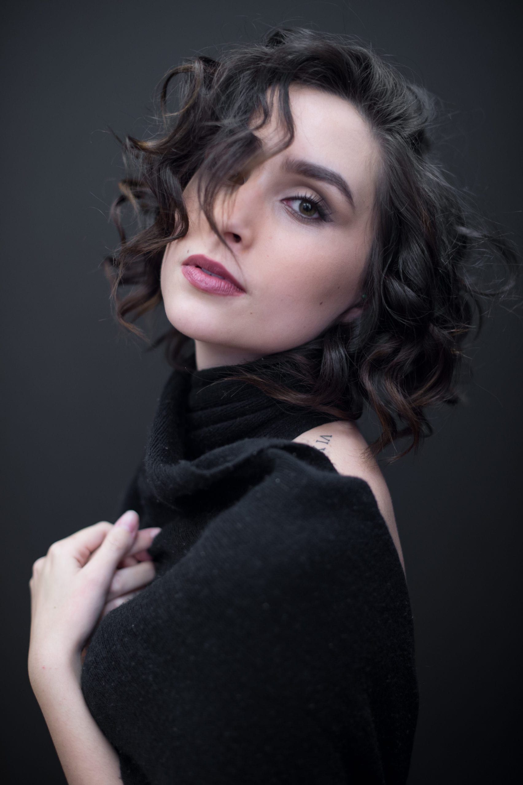 Woman with curly dark hair and deep red lipstick in a black sweater, looking at the camera.