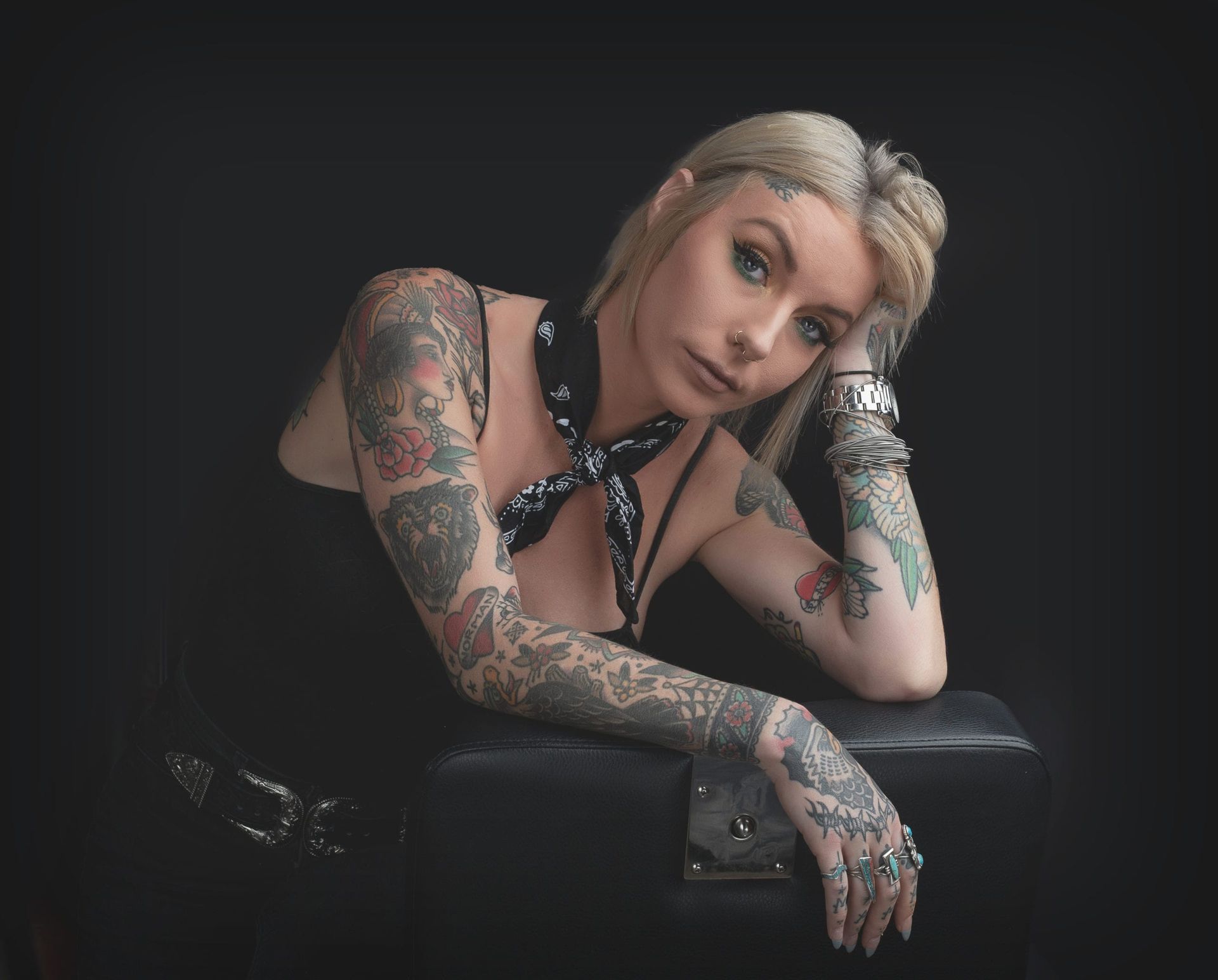 Woman with tattoos, leaning on a black surface, wearing a bandana and looking at the viewer.