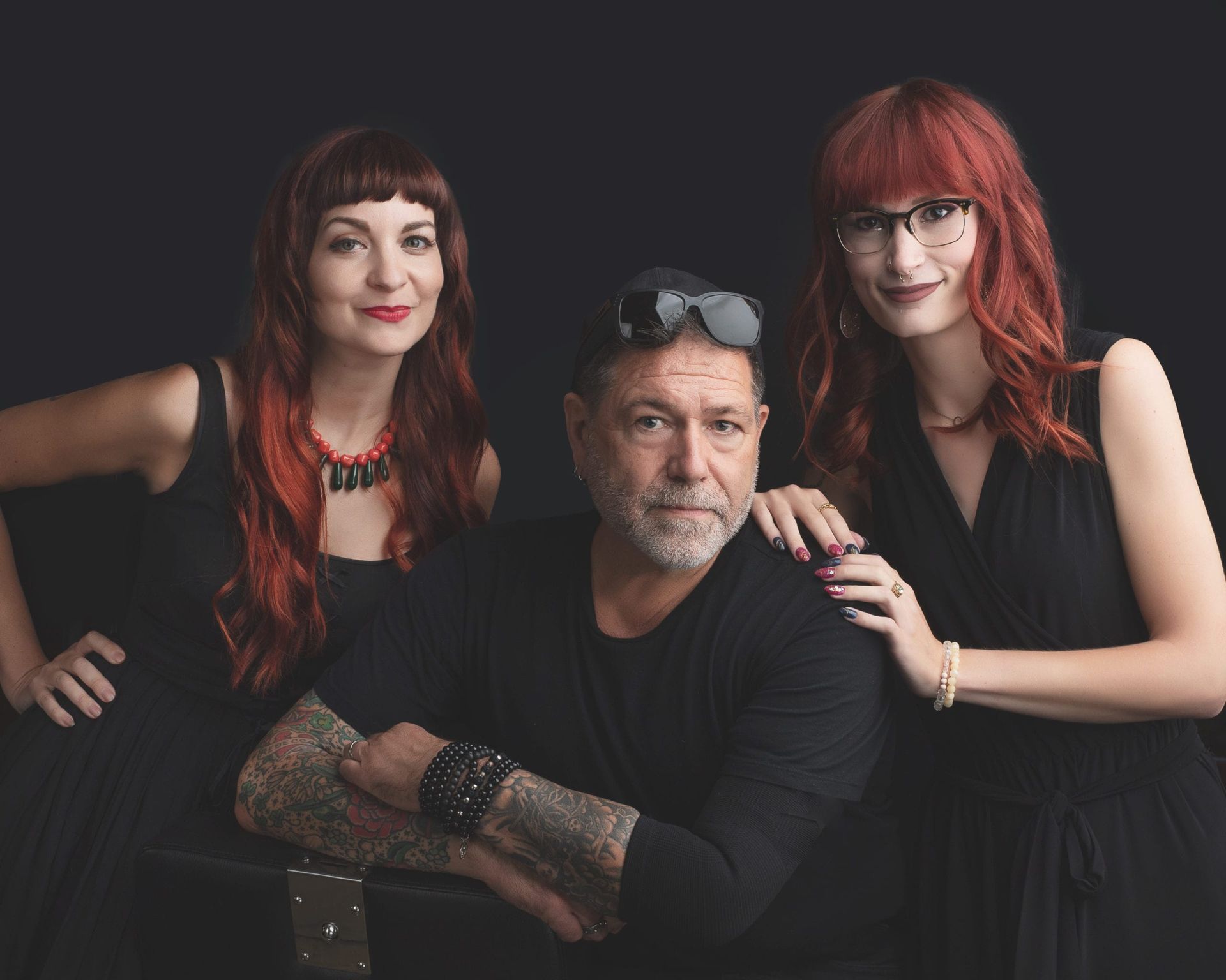 Three people posing, two women and a man, with red hair against a black backdrop.