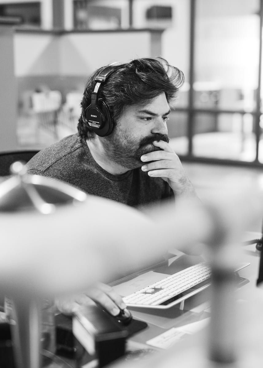 Man with headphones, working on a computer, using a mouse, in an office setting, with a concerned expression.