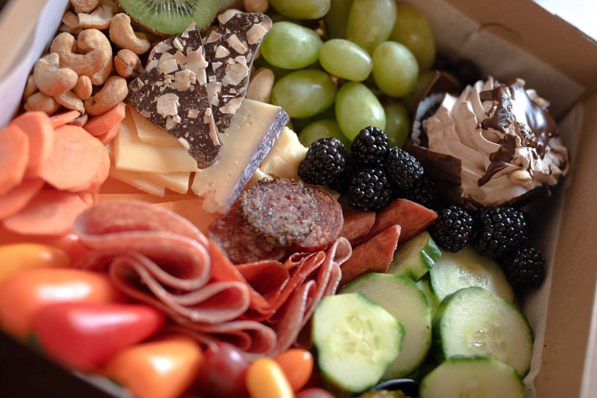 Charcuterie box with colorful fruits, vegetables, meats, nuts, cheese, and chocolate treats.