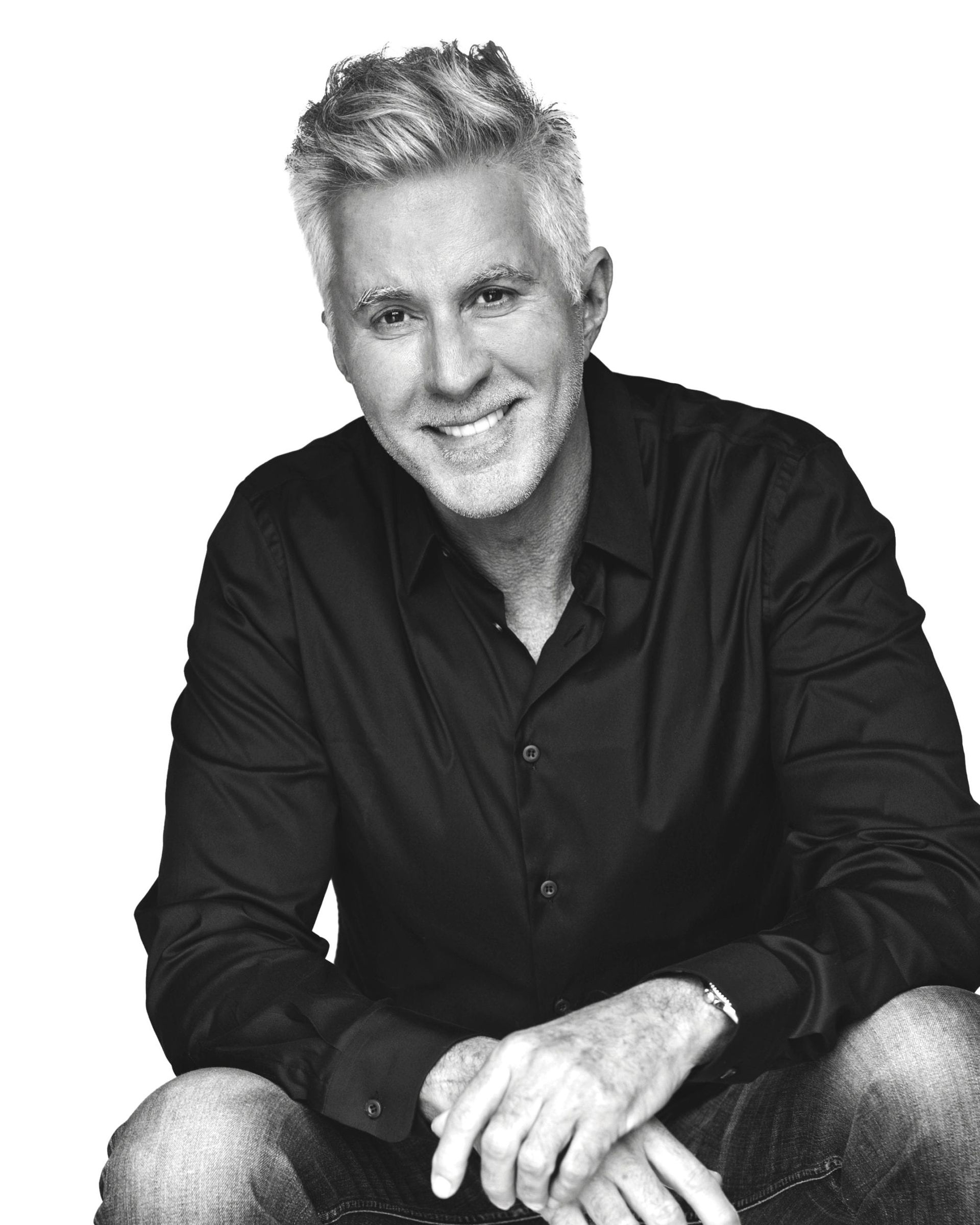 Man with gray hair smiling, wearing a black button-down shirt and jeans.
