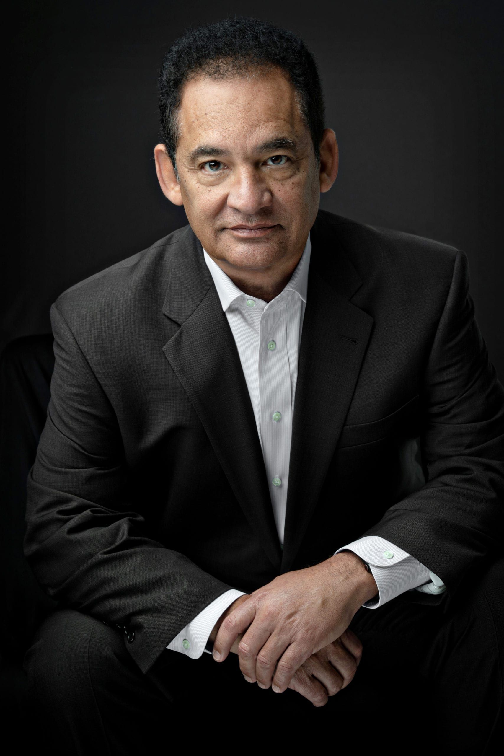 Man in suit, arms crossed, looking at the camera, dark background.