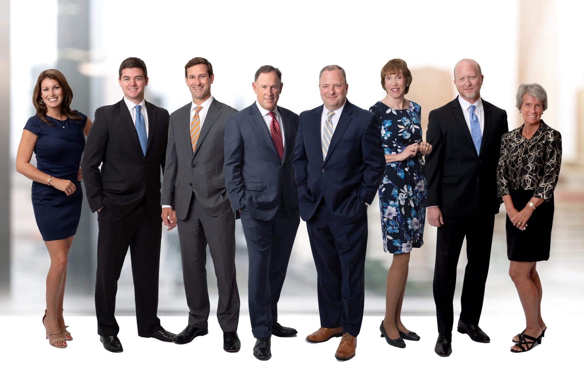Group of nine professionals in business attire posing for a photo in a modern office setting.